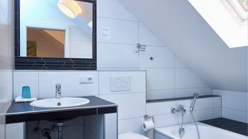 A modern bathroom with a skylight, a sink, a toilet, and a bathtub.