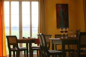 Un comedor con una mesa dispuesta para dos personas, dos copas de vino y vistas a un paisaje verde a través de amplios ventanales.