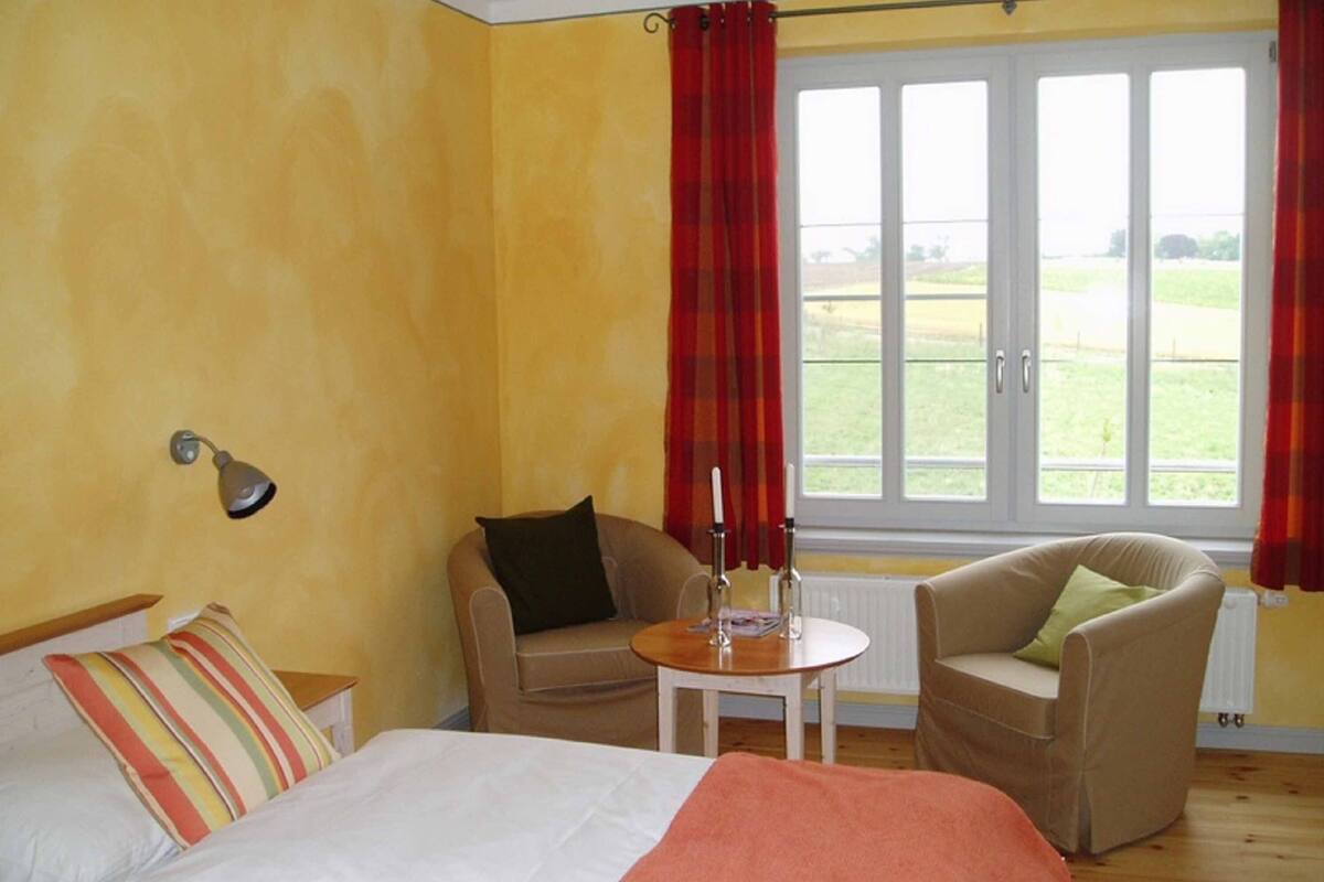 A bedroom with a bed, two chairs, a small table, and a window with curtains.
