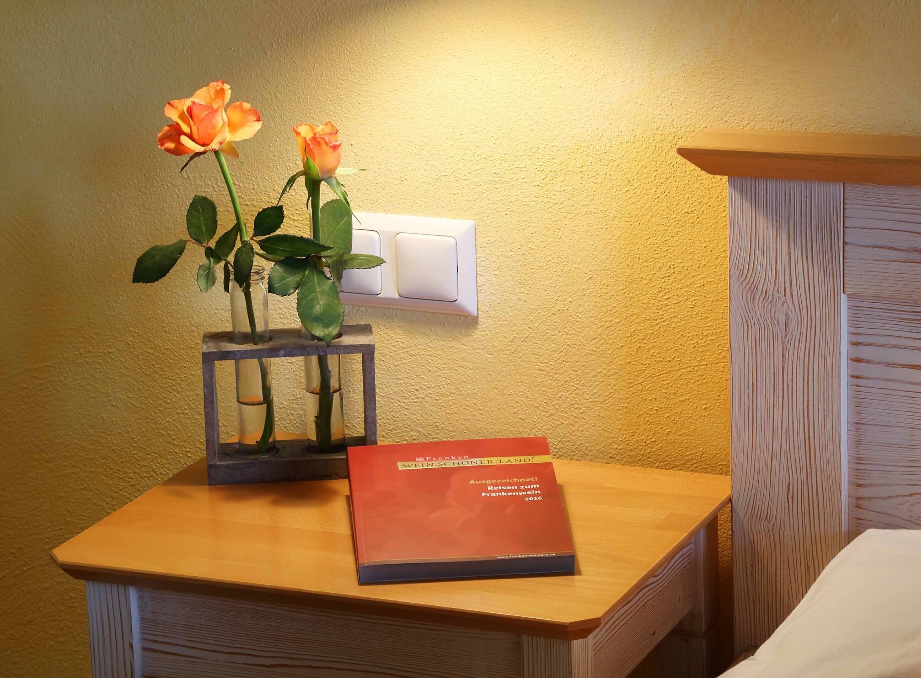 A bedside table with a vase of roses and a book titled "Frankenstein".