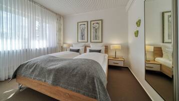 Una habitación de hotel con una cama grande, dos mesitas de noche, un espejo y una ventana con cortinas translúcidas.