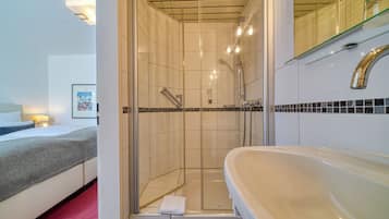 A hotel bathroom with a shower, a sink, and a bed with a red carpet.