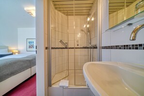 A hotel bathroom with a shower, a sink, and a bed with a red carpet. - Ostseeresidenz Cammann (Groemitz)