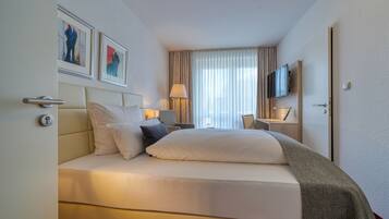 A hotel room with a bed, a television, a desk, and artwork on the wall.
