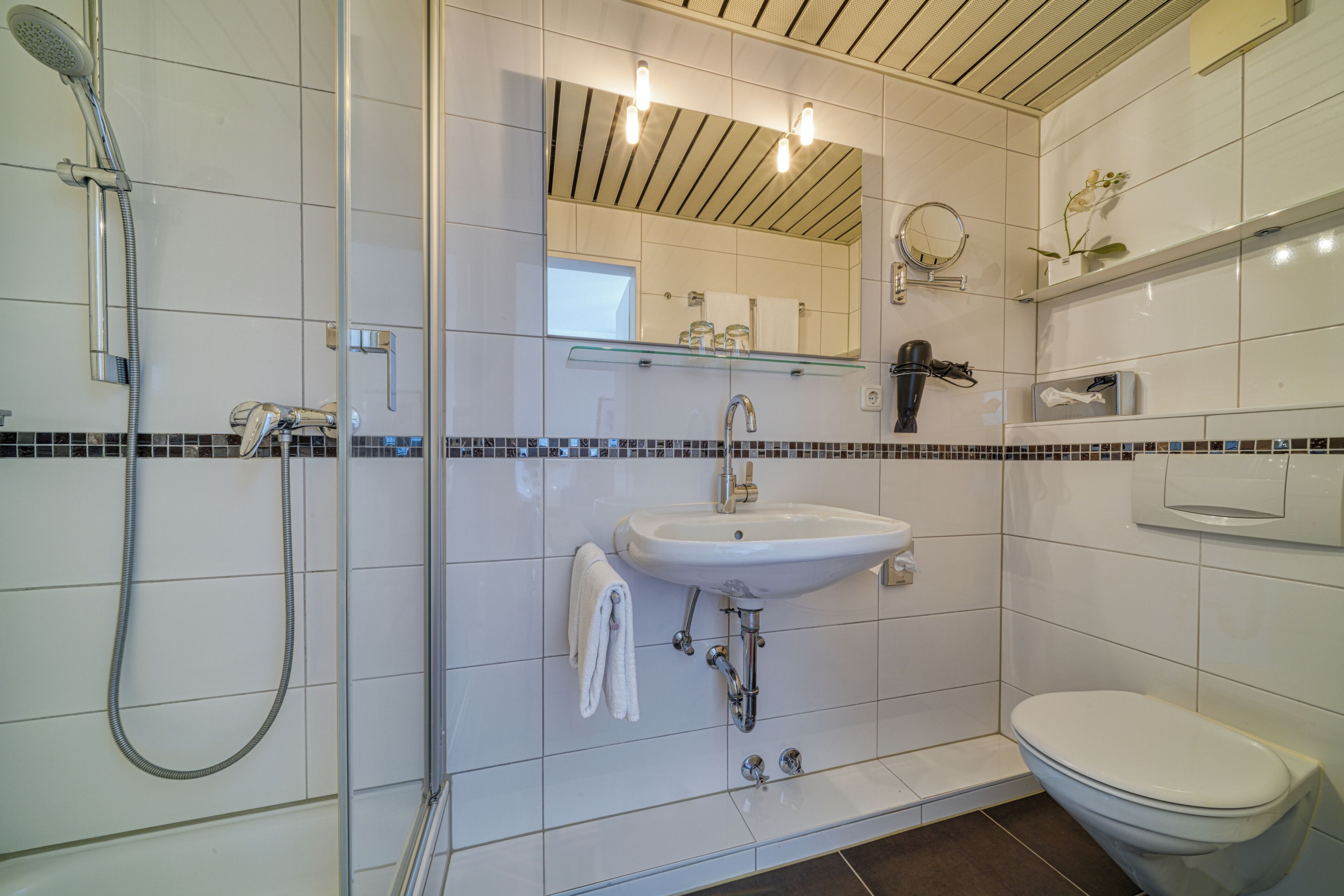 Une salle de bain moderne avec une douche à parois de verre, un lavabo blanc, des toilettes et un miroir avec des lumières au-dessus.
