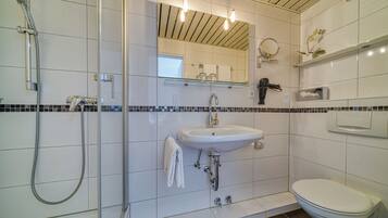 Une salle de bain moderne avec une douche à parois de verre, un lavabo blanc, des toilettes et un miroir avec des lumières au-dessus.