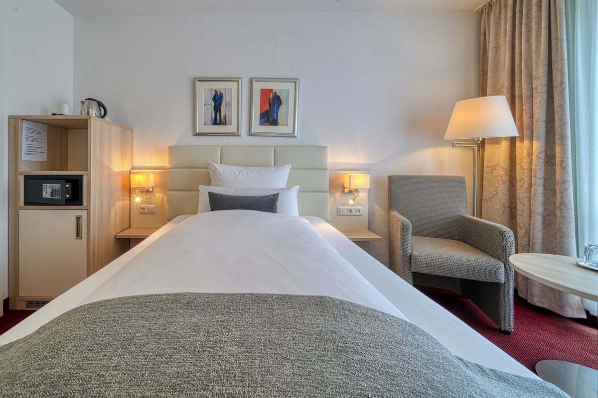 A hotel room with a bed, a desk, a chair, a lamp, a small table, and a cabinet.