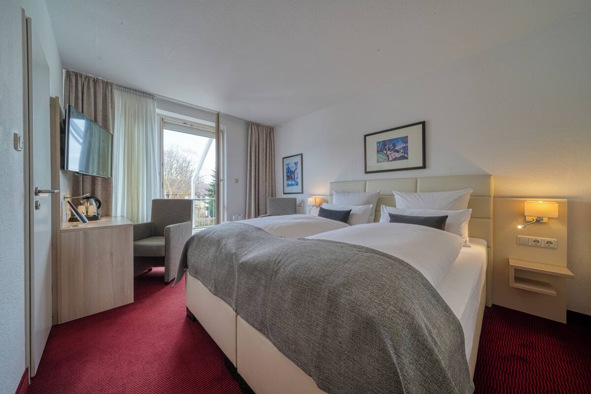 A hotel room with a bed, a desk with a TV, a chair, and a window.