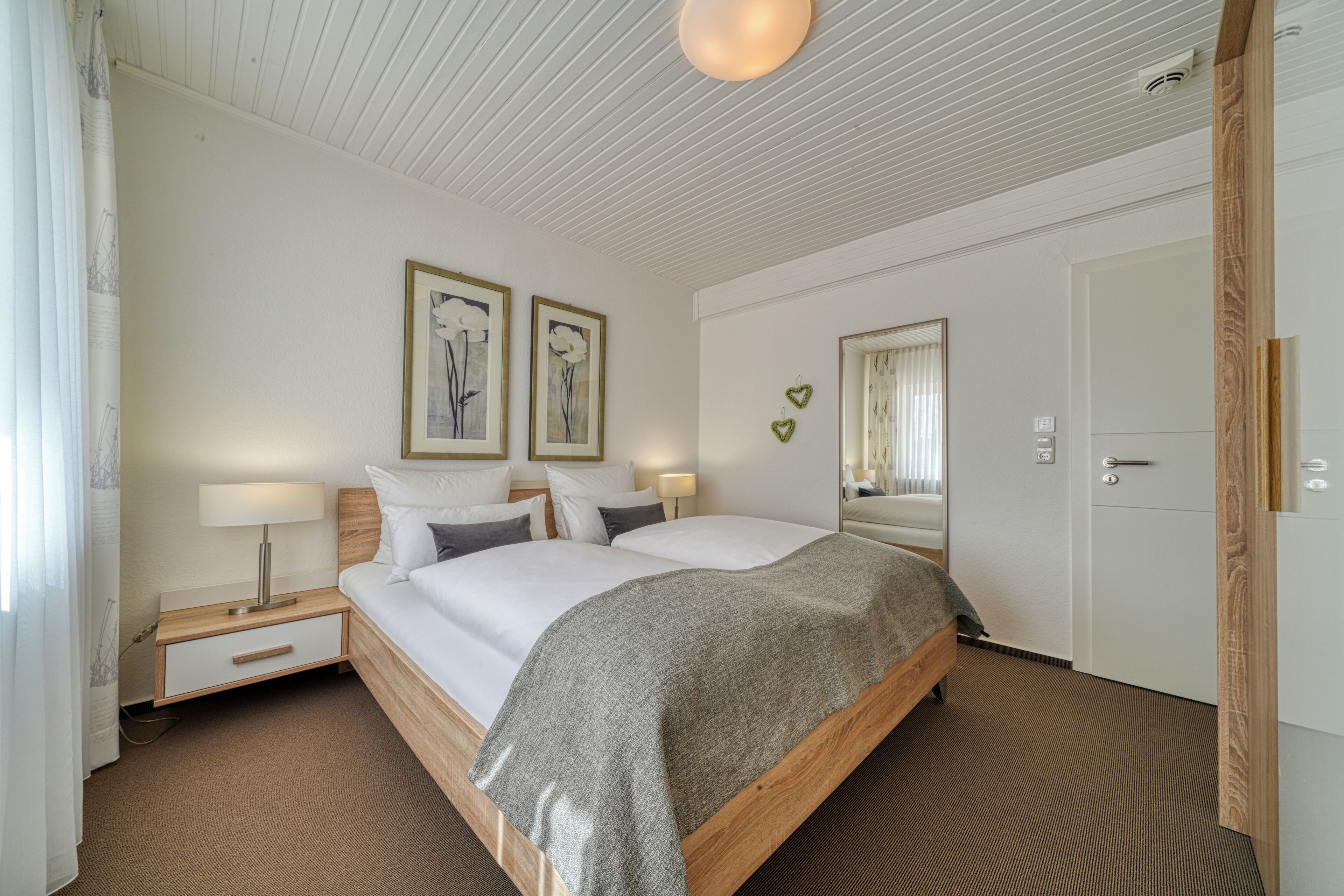 A neatly arranged bedroom with a bed, bedside tables, lamps, and framed artwork on the wall.