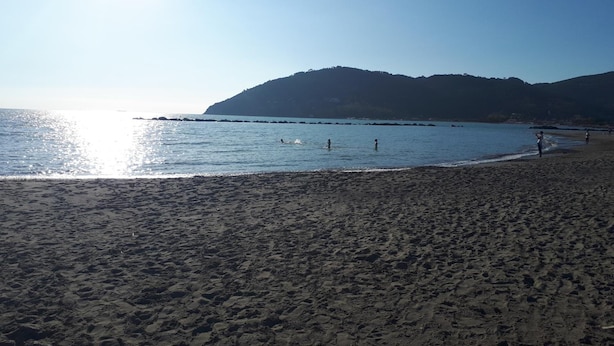 Una platja amb cel blau, aigua tranquil·la i un turó allunyat.