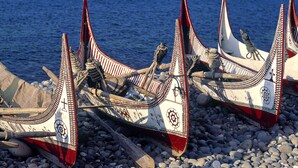 Several traditional boats with decorative patterns, docked on a rocky shore by the sea. - Tahabi Shoe Store (Wazirpur)