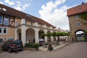 A courtyard with outdoor seating, a stone building, and a car parked on the side.
