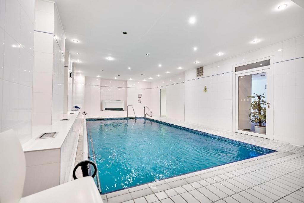 A modern indoor swimming pool with clear water, surrounded by white tiled walls and a ceiling with recessed lighting.