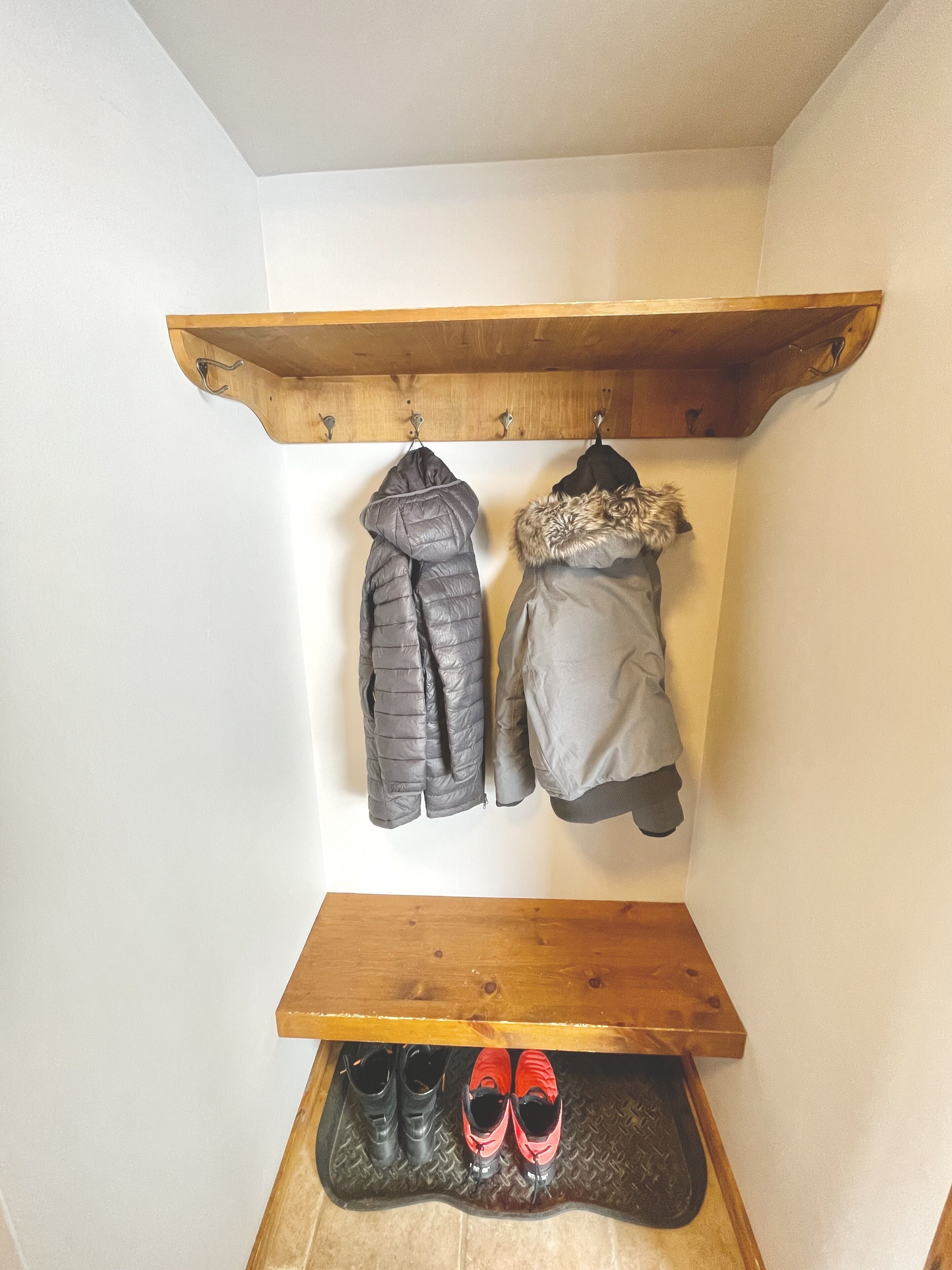 Een houten kapstok met twee jassen en een paar rode schoenen op een plank.