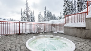 A hot tub in a snowy outdoor area with a red fence and snow-covered trees in the background. - Newly Renovated Ground Floor Creekside Studio Condo - Pet Friendly too!  (Silver Star Mountain)