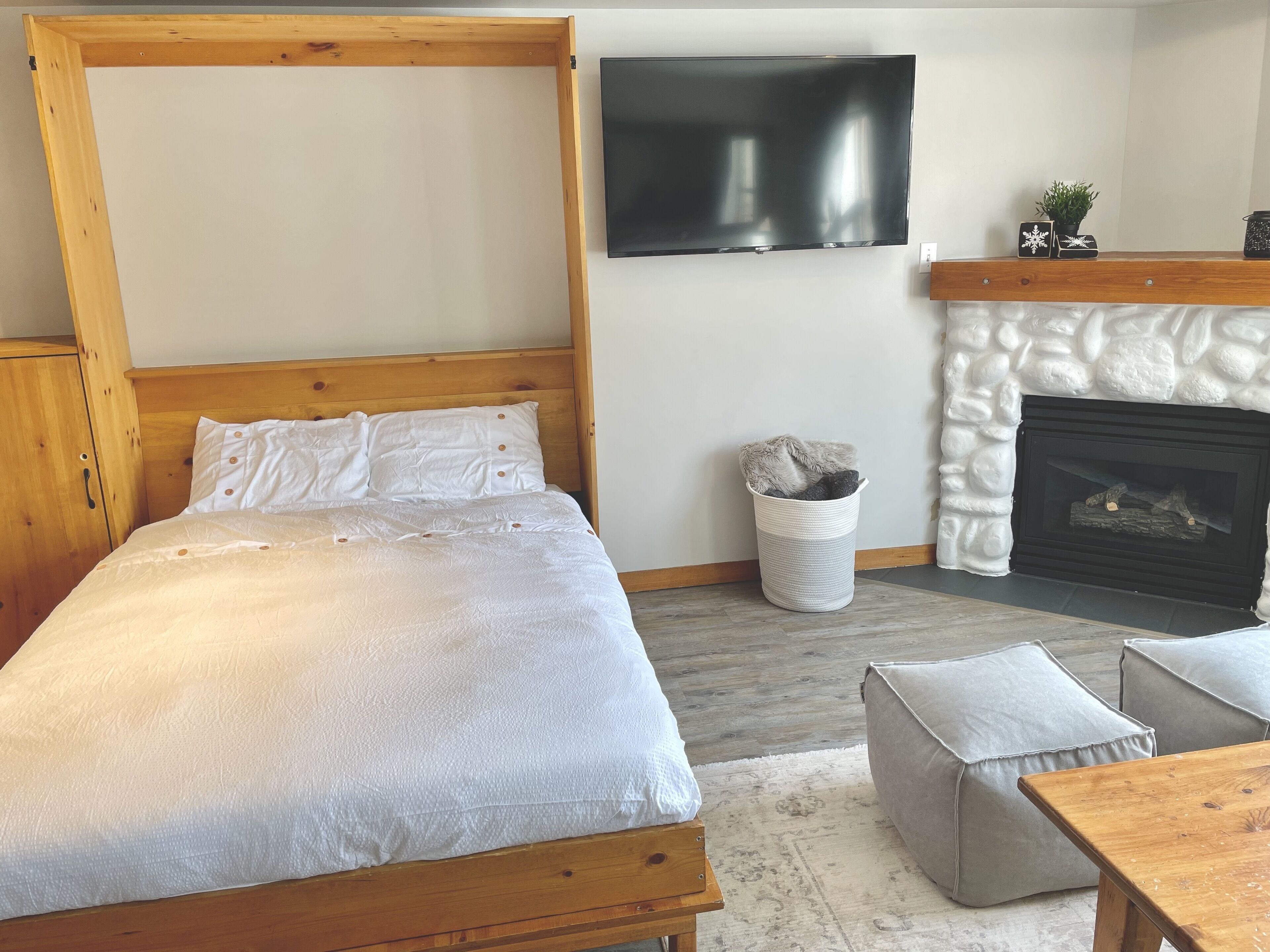 A bedroom with a wooden four-poster bed, a television mounted on the wall, a stone fireplace, and a small waste basket.