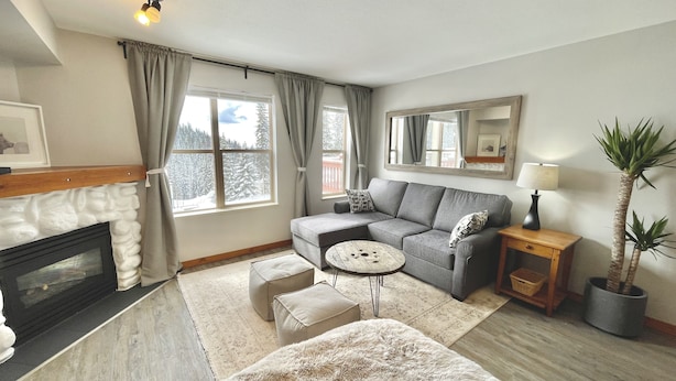 A cozy living room with a fireplace, a grey sofa, a round coffee table, and a large mirror. - Newly Renovated Ground Floor Creekside Studio Condo - Pet Friendly too!  (Silver Star Mountain)