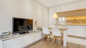 A modern kitchen with white cabinetry, a wooden countertop, and a built-in TV. There are two white chairs and a dining table. - Happy InnSide in central. Self check-in + free parking (Vilnius)
