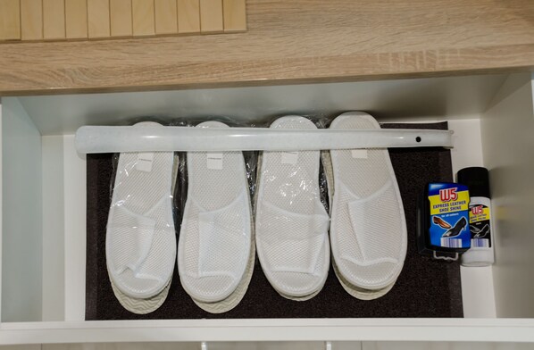 A storage drawer containing four pairs of white slip-on shoes, a shoe shine kit, and a wooden cabinet above.