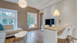 A modern living room with a sofa, a dining area with a table and chairs, a TV, and large windows. - Happy InnSide in central. Self check-in + free parking (Vilnius)