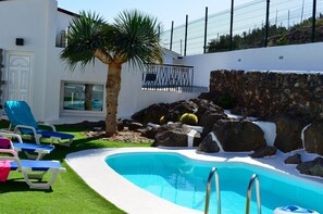 A pool area with a palm tree, lounge chairs, and a stone wall. - Beautiful villa located in Ingenio, in the southeast of Gran Canaria. (Ingenio)