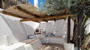 Un espace extérieur ensoleillé, aménagé avec une pergola, des bancs rembourrés et un petit arbre.