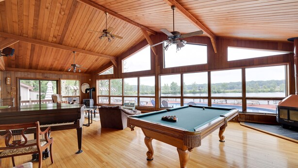 A spacious room with a pool table, wooden flooring, and large windows offering a view of the outdoors. - Pocono Lakefront Paradise, dock, hot tub, private pool and tennis court (pocono summit)