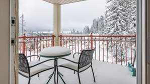 Un balcon avec une table et des chaises, donnant sur un paysage enneigé parsemé d’arbres.