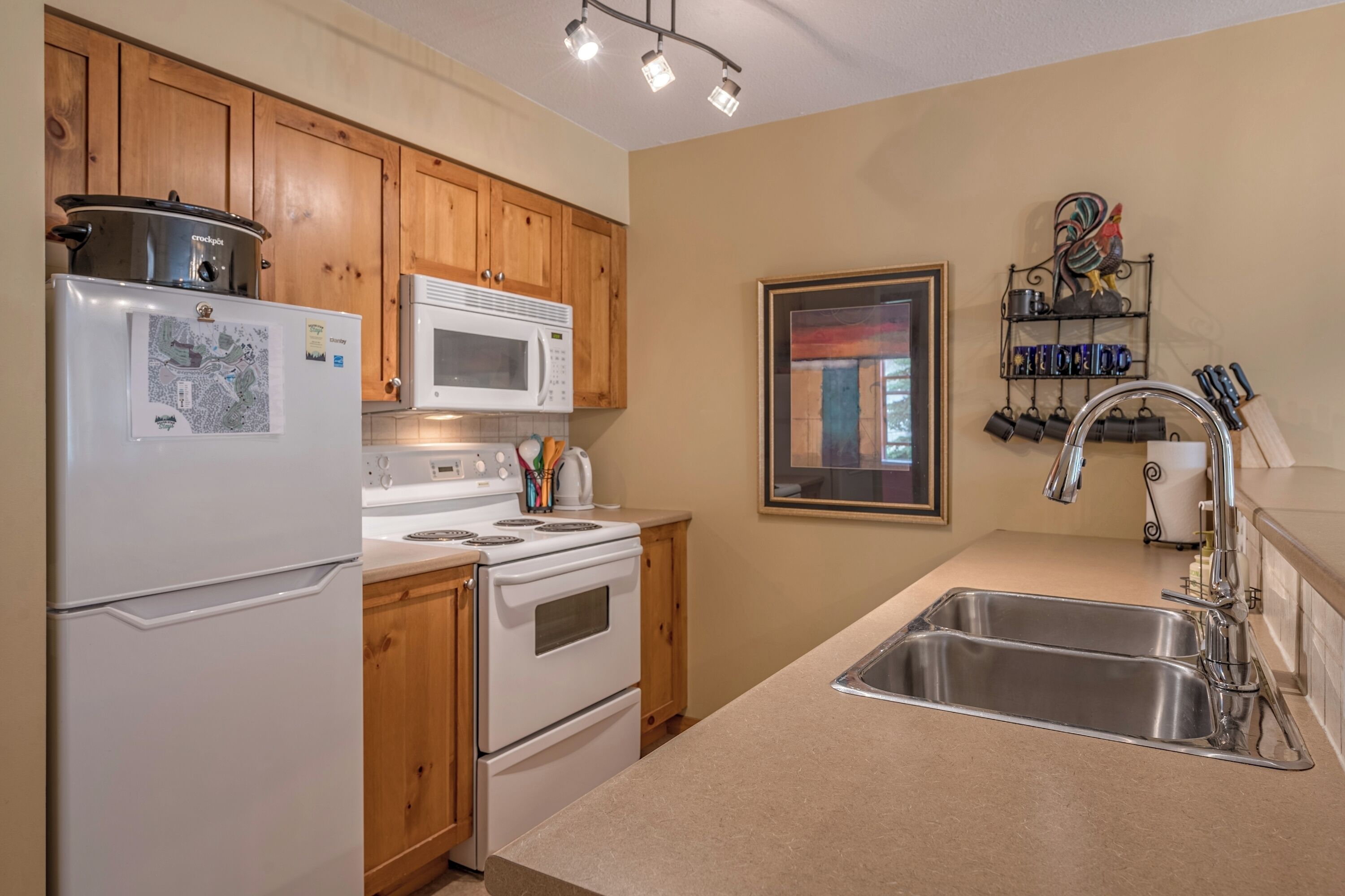 A kitchen with wooden cabinets, a white refrigerator, a microwave, a stove, and a sink.