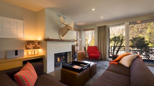 Una sala de estar moderna con chimenea, un sillón rojo, un sofá y un amplio ventanal con vistas a árboles.