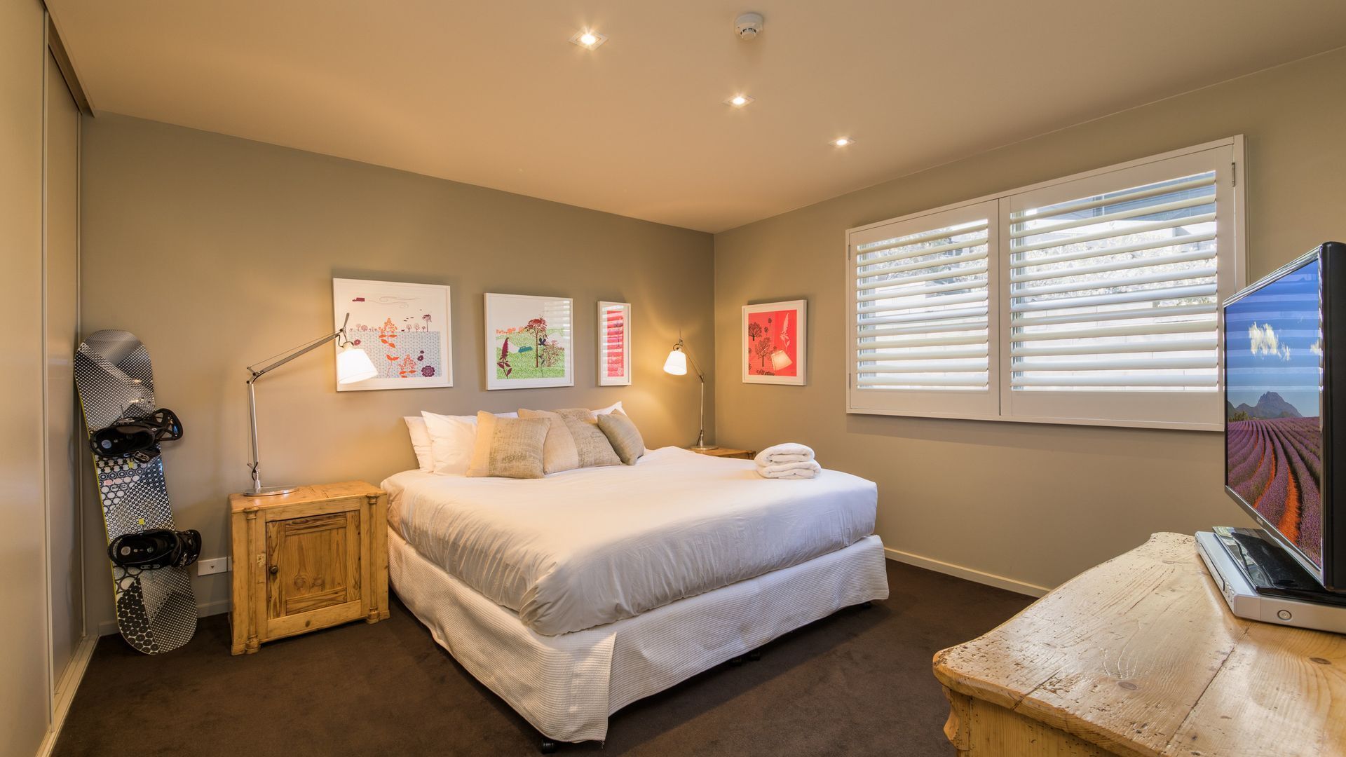 A bedroom with a bed, a nightstand, a lamp, a TV, and artwork on the wall.