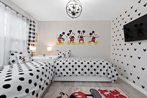 Une chambre avec deux lits, un autocollant mural à l’effigie de Mickey Mouse, un lustre et un téléviseur fixé au mur.