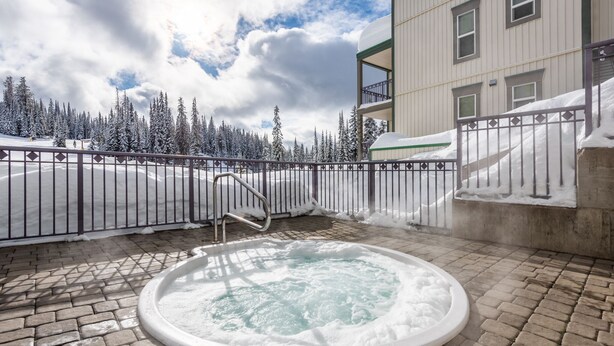 A hot tub surrounded by a metal fence, with a snowy landscape and a building in the background.