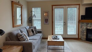 A living room with a gray sofa, a wooden coffee table, a fireplace, and a stone wall.