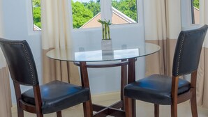 A room with a glass table and two chairs, a window with curtains, and a view of greenery outside. - Tropical Luxury Dreams Ocho Rios (Ocho Rios)