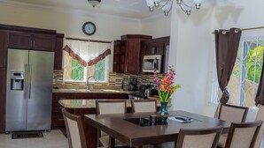 A modern kitchen with dark wooden cabinets, a stainless steel refrigerator, and a dining area with a table and chairs. - Tropical Luxury Dreams Ocho Rios (Ocho Rios)