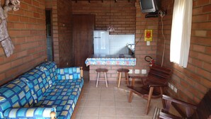 A small, enclosed room with a brick wall, a blue patterned sofa, a wooden table with stools, and a television mounted on the wall. - Bangalôs Canto das Águas, waterfall with natural pool (Paraty)