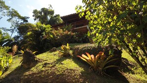 A lush garden with various plants and a wooden building in the background. - Bangalôs Canto das Águas, waterfall with natural pool (Paraty)