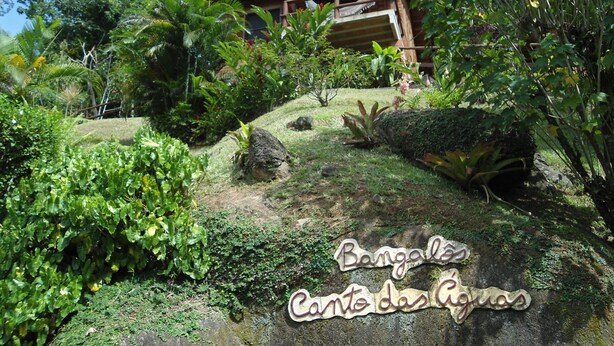 A rustic wooden building with a sloped roof, surrounded by lush greenery and a stone pathway. - Bangalôs Canto das Águas, waterfall with natural pool (Paraty)