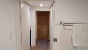 A narrow hallway with a wooden door at the end, a towel rack on the right, and a light switch on the left. - Fully-furnished, family & pet-friendly home 100m the water.. (wynnum)