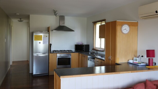 A compact kitchen with a refrigerator, stove, microwave, oven, and a wooden cabinet with a clock. - Fully-furnished, family & pet-friendly home 100m the water.. (wynnum)
