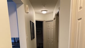 A hallway with a patterned rug, white walls, and a door leading to another room.