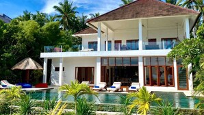 A two-story house with a swimming pool, surrounded by tropical vegetation.