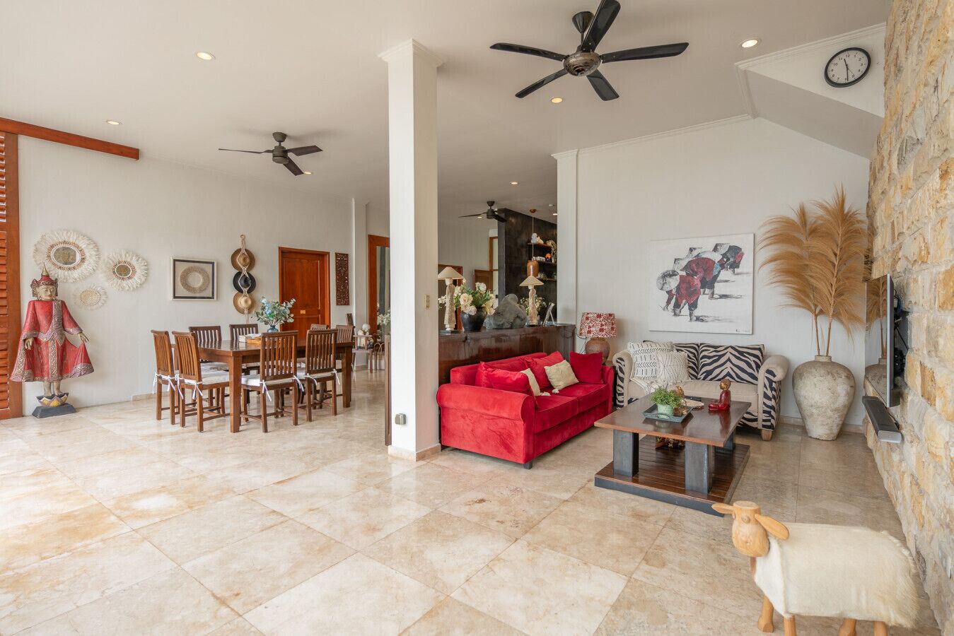 A spacious living area with a red sofa, a wooden dining table, and a ceiling fan.