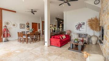 A spacious living area with a red sofa, a wooden dining table, and a ceiling fan.