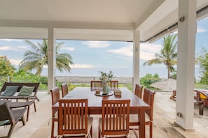 Enjoy al fresco dining with ocean views from this outdoor dining area, featuring a table and chairs, a wicker sofa, and a thatched umbrella.