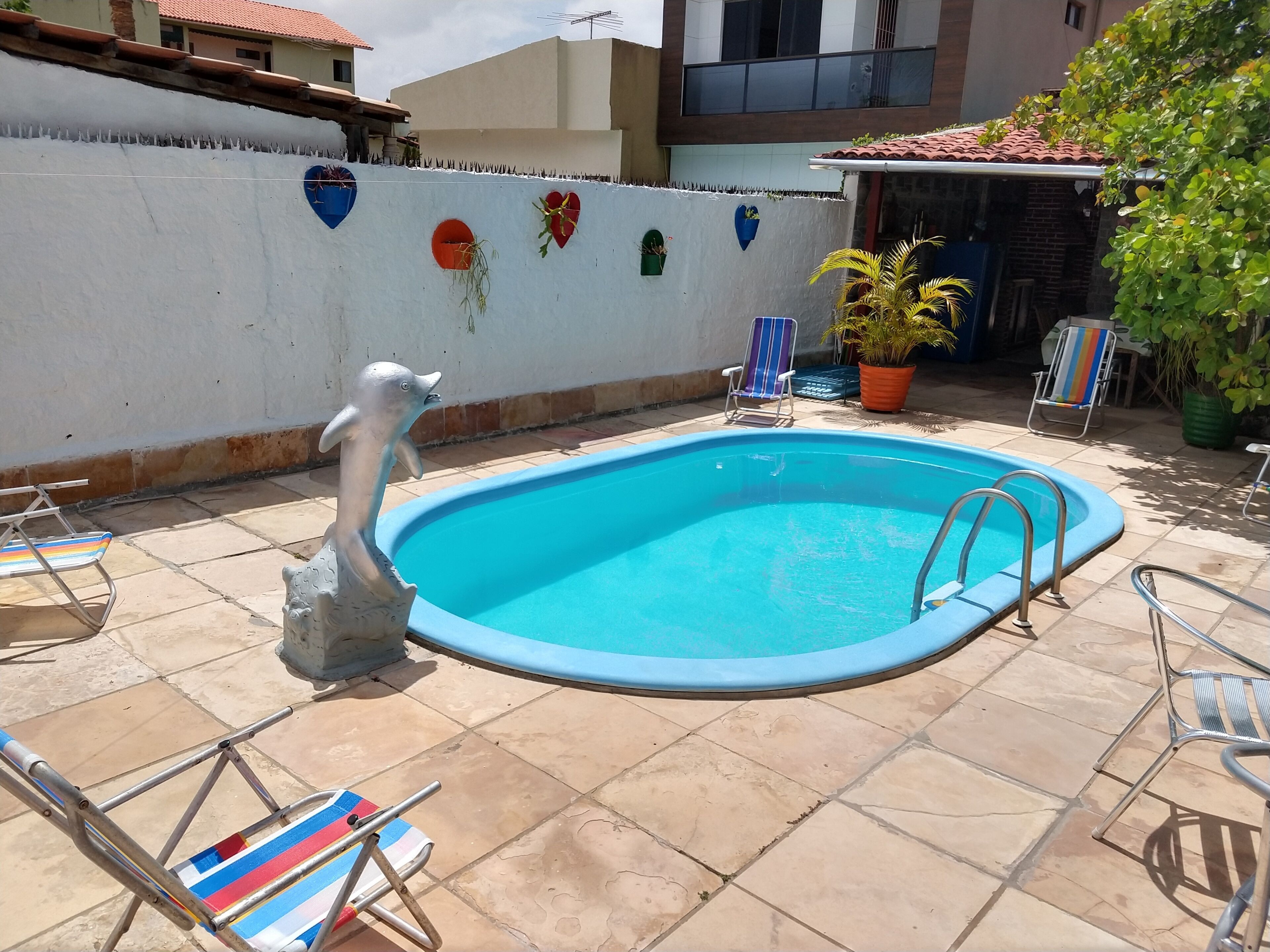 A swimming pool with a decorative dolphin statue, surrounded by tiled patio and lounge chairs.