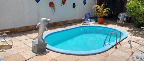 A swimming pool with a decorative dolphin statue, surrounded by tiled patio and lounge chairs.