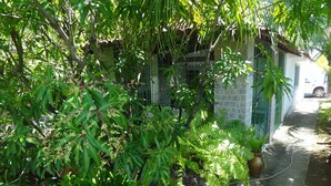 A garden area with various plants and a pathway leading to a building with a metal gate. - Casa em Porto de Galinhas. 450m aproximado da praia. Piscina com apoio coberto (Porto de Galinhas)