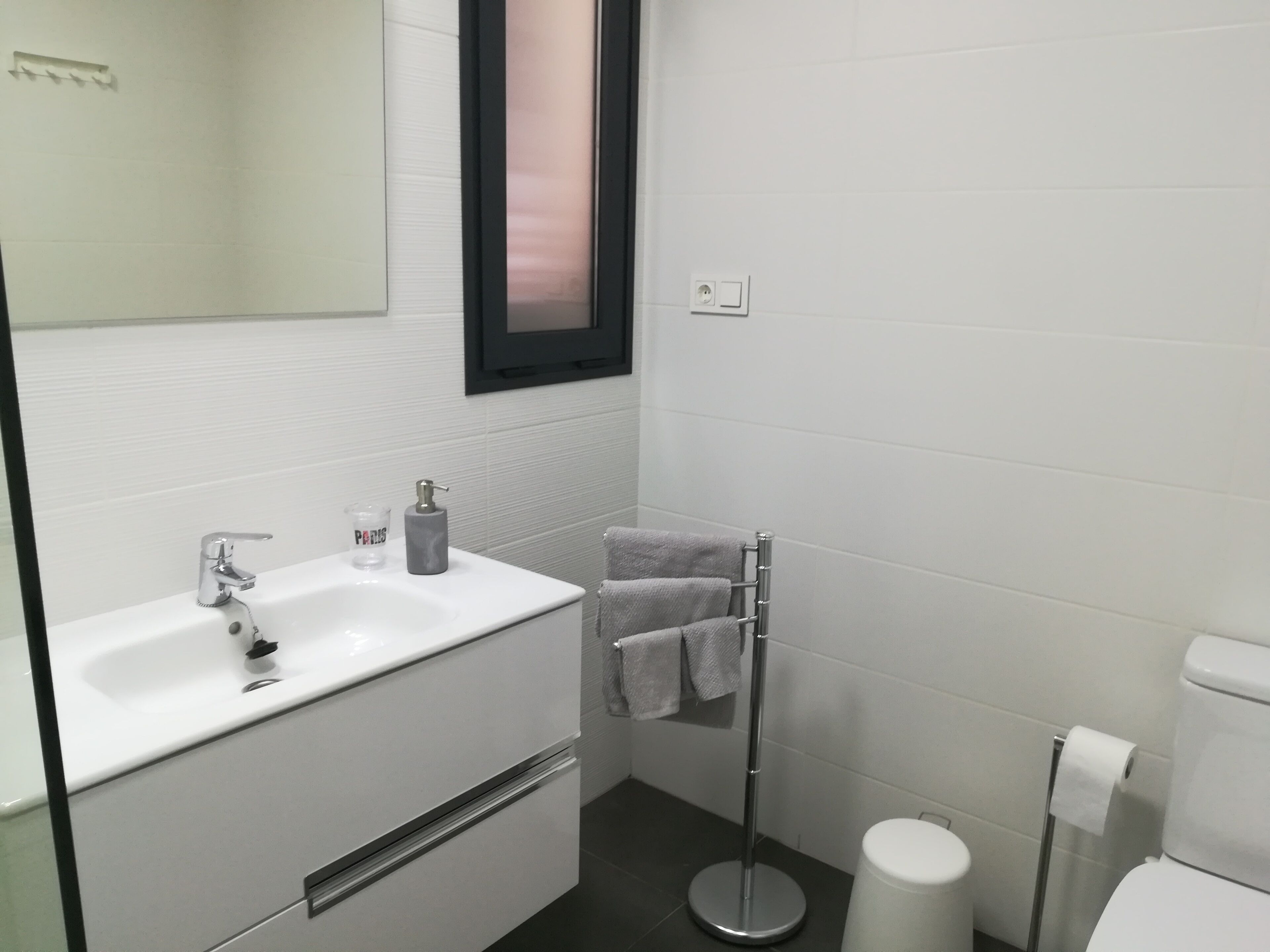 Een moderne badkamer met een witte wastafel, een spiegel, een handdoekhouder en een toilet.